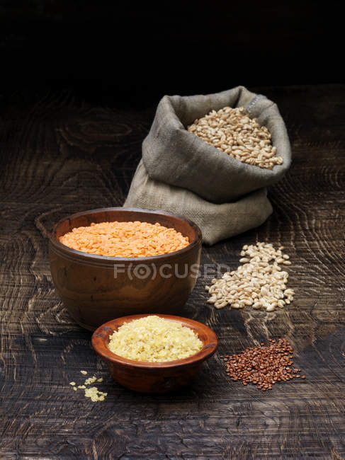 Still life with bowls of red lentils and grains with sack of seeds — Stock Photo