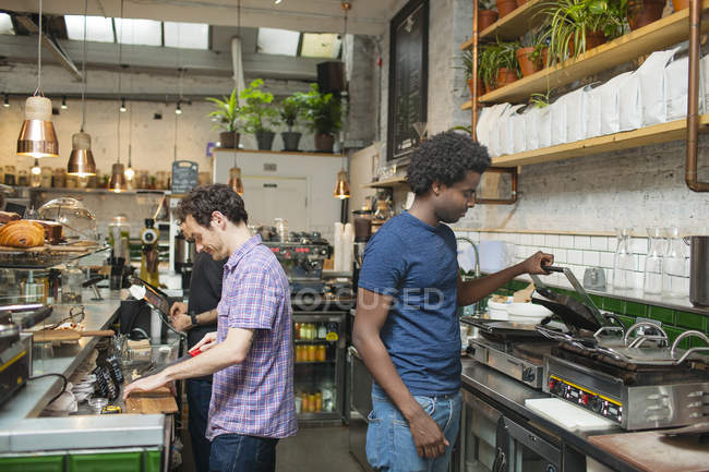 Dos camareros preparando comida en la cocina de la cafetería - foto de stock