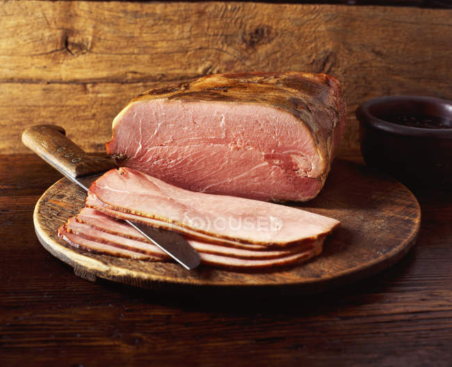 Partly sliced honey roast ham on wooden chopping board — Stock Photo