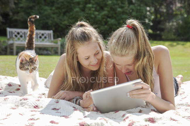 Zwei Teenager-Mädchen blicken auf digitales Tablet auf Picknickdecke — Stockfoto