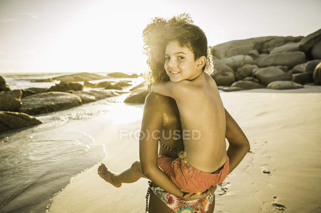 Mother giving son piggyback ride on beach — Stock Photo