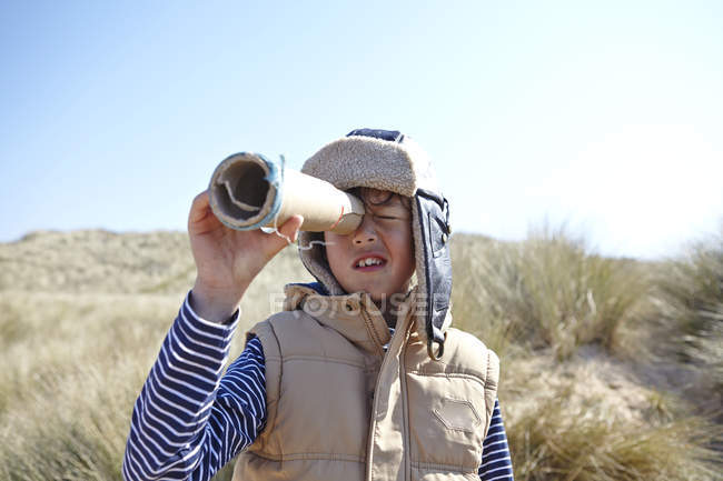 Мальчик на пляже, смотрит через воображаемый телескоп — стоковое фото