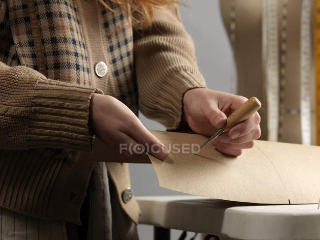Cropped close up of young female fashion designer piercing dressmaker pattern — Stock Photo