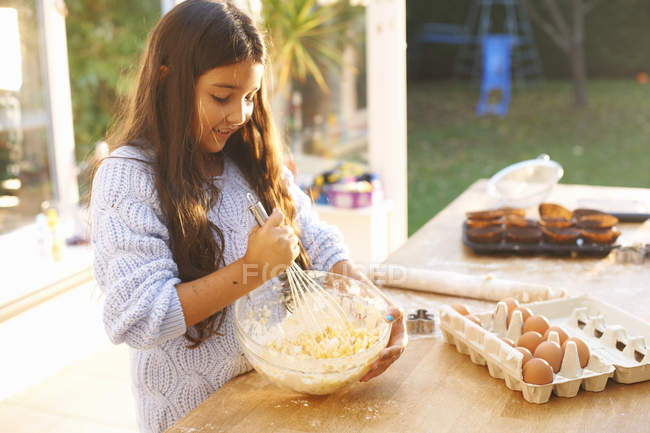Chica batiendo mezcla en tazón en la cocina en casa - foto de stock