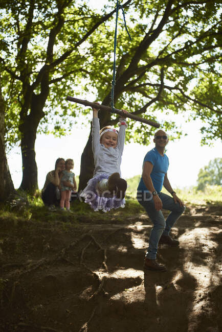 Молода дівчина гойдається на дереві, поки її сім'я дивиться — стокове фото