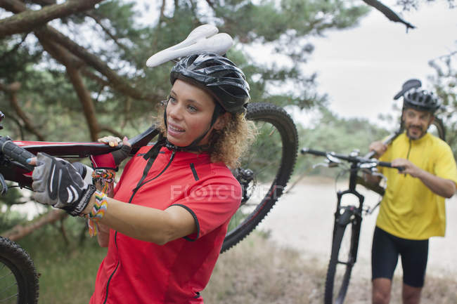 Mountain biking couple carrying cycles over sand on riverbank — Stock Photo