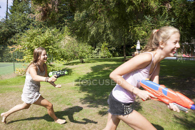 Дві дівчинки-підлітки біжать з водяними гарматами в саду — стокове фото