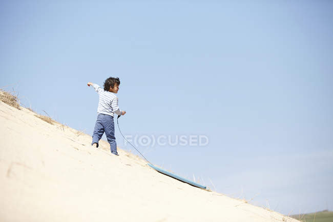 Молодий хлопчик з санчатами на піщаному пагорбі — стокове фото