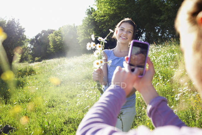 Girl taking photo of sister with picking flowers — Stock Photo