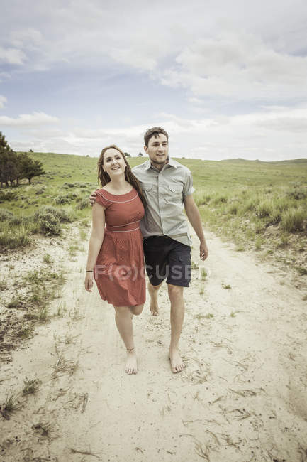 Jeune couple marchant pieds nus le long d'une piste sablonneuse, Cody, Wyoming, USA — Photo de stock