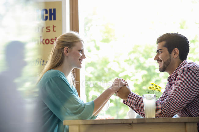 Side view of couple holding hands across table, looking at each other smiling — Stock Photo