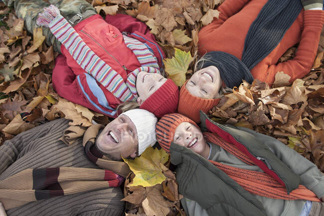 Сім'я лежить разом в осінньому листі, сміючись — стокове фото