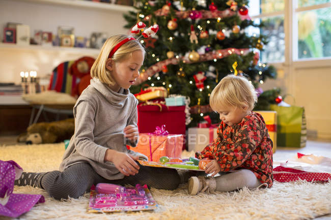 Irmãs verificando presentes pela árvore de Natal — Fotografia de Stock