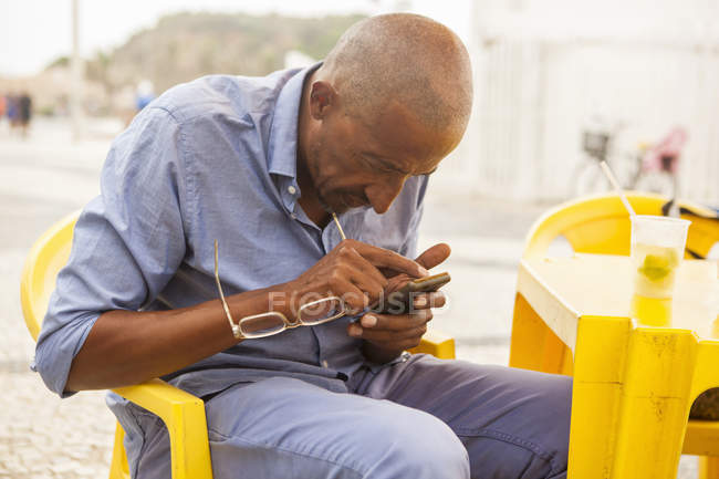 Hombre maduro concentrándose en el teléfono inteligente en el bar en la playa de Ipanema, Río de Janeiro, Brasil - foto de stock