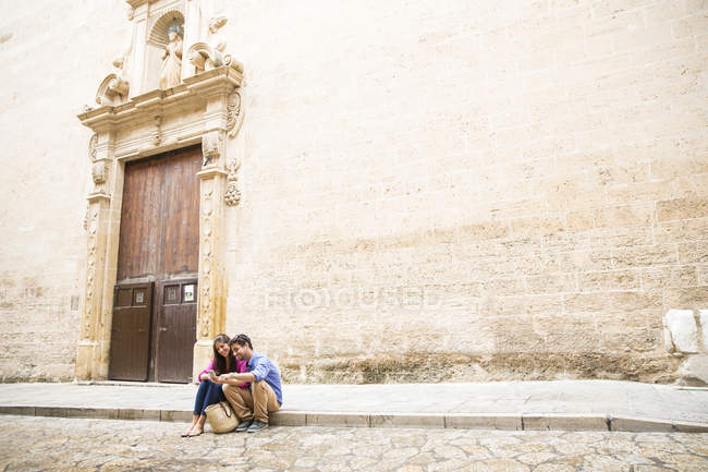 Pareja usando teléfono móvil en pavimento, Palma de Mallorca, España - foto de stock