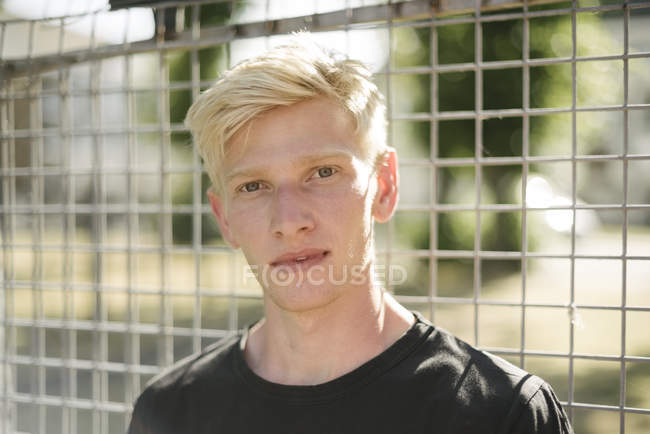 Portrait of blond haired young man by wire fence — Stock Photo