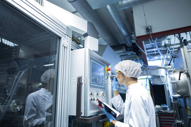 Científico masculino con panel de control de ajuste portátil en sala limpia de laboratorio - foto de stock