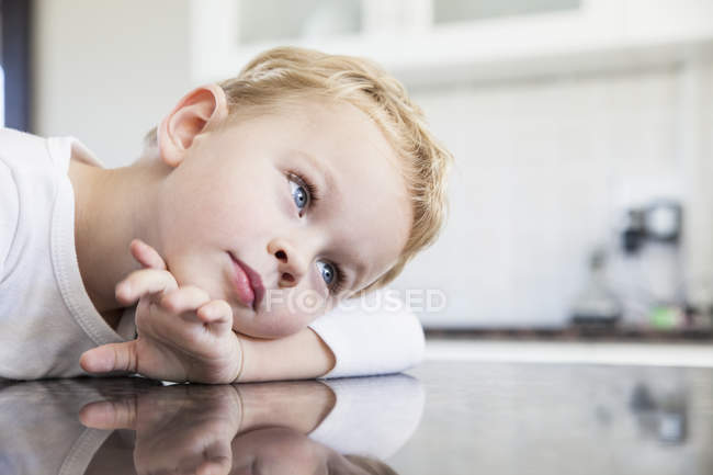 Retrato del niño preescolar apoyado en el banco de la cocina - foto de stock
