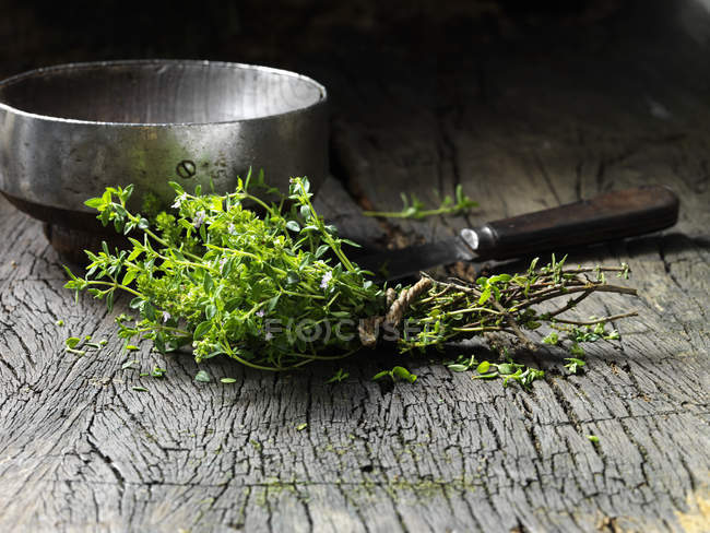 Thymianblätter mit Schnur, Metallschale und Messer auf rustikaler Holzoberfläche zusammengebunden — Stockfoto