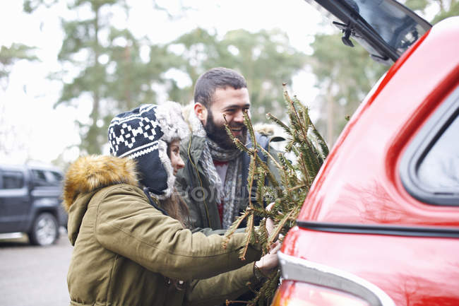 Jeune couple avec arbre de Noël dans la botte de voiture — Photo de stock