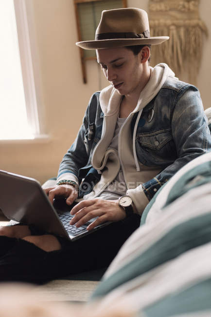 Hombre joven relajándose en casa, utilizando el ordenador portátil - foto de stock