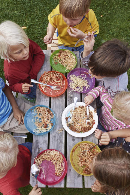 Overhead view of seven children eating spaghetti at picnic table — Stock Photo