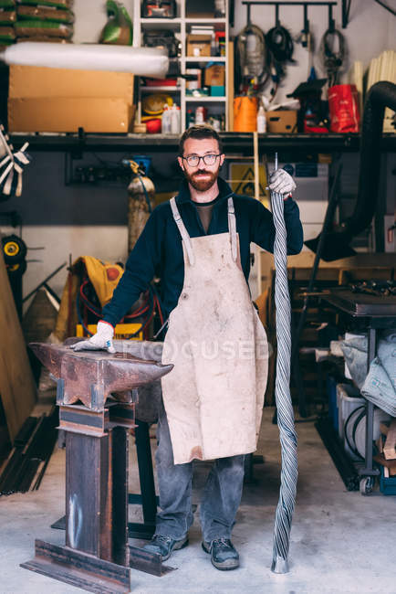 Porträt eines Metallarbeiters, der in der Schmiedewerkstatt am Amboss lehnt — Stockfoto