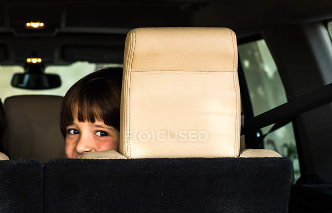 Portrait of happy boy looking over his shoulder from car back seat — Stock Photo