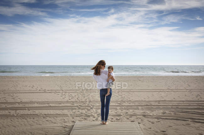 Vista posteriore della donna che porta la figlia del bambino sulla spiaggia, Castelldefels, Catalogna, Spagna — Foto stock