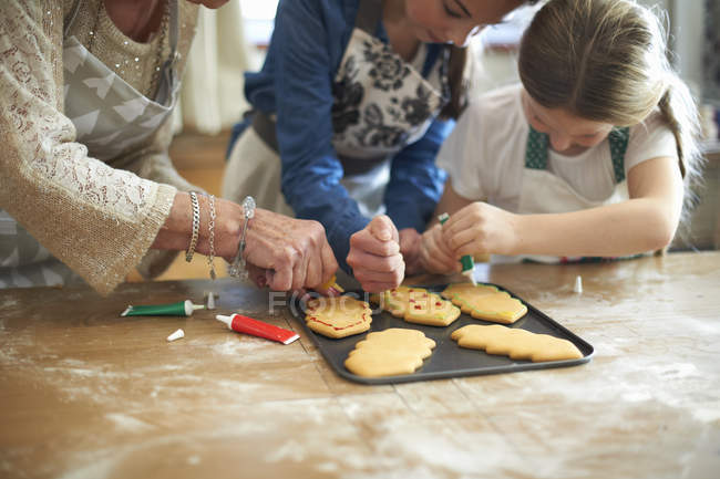 Обрезанный снимок пожилой женщины и внучек, украшающих рождественское печенье — стоковое фото