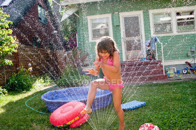Chica joven jugando en aspersor de jardín - foto de stock