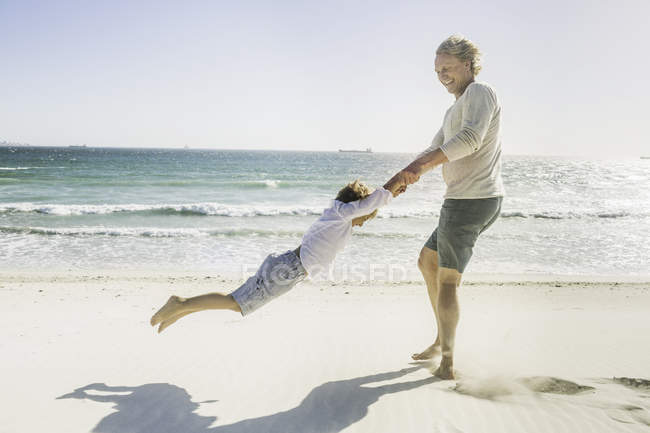 Отец размахивает сыном на пляже — стоковое фото