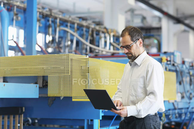 Gestionnaire technique vérifiant les informations sur l'ordinateur portable dans l'usine — Photo de stock