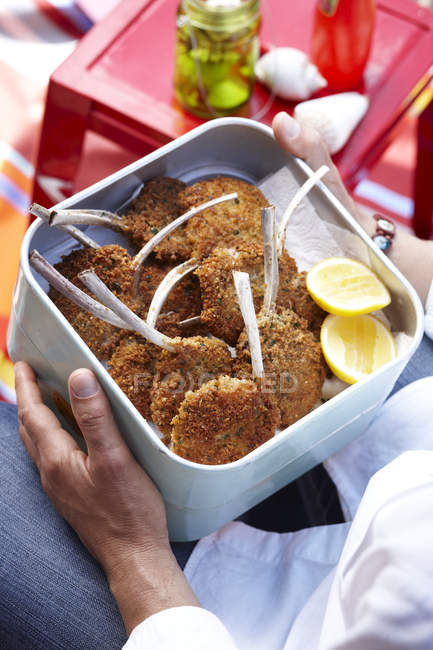 Cropped image of mid adult man holding container of parmesan lamb cutlets — Stock Photo