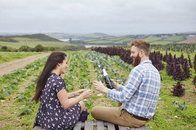 Paar in ländlicher Umgebung sitzt auf Paletten und schenkt Champagner ein — Stockfoto