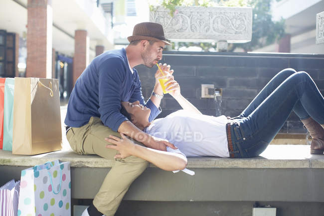 Середня доросла пара відпочиває на сидінні, п'є напій, торгує сумками поруч з ними — стокове фото