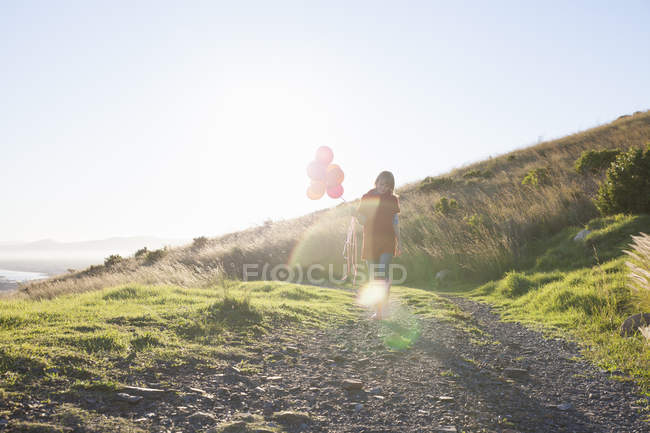 Young woman strolling along dirt track with bunch of balloons — Stock Photo