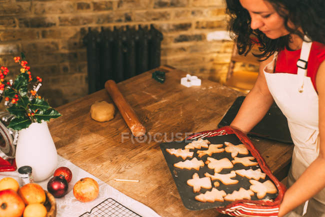 Mature woman carrying fresh Christmas cookies to kitchen counter — Stock Photo