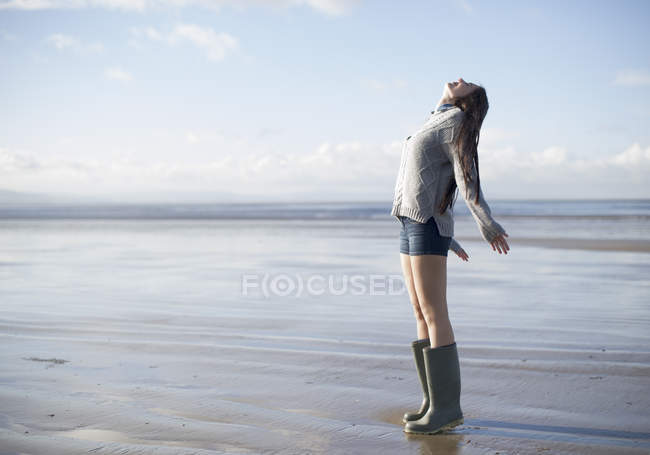 Mujer joven de pie en la playa mirando hacia arriba, Brean Sands, Somerset, Inglaterra - foto de stock