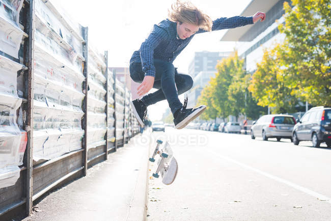 Jeune skateboarder urbain masculin faisant saut de skateboard sur la route — Photo de stock