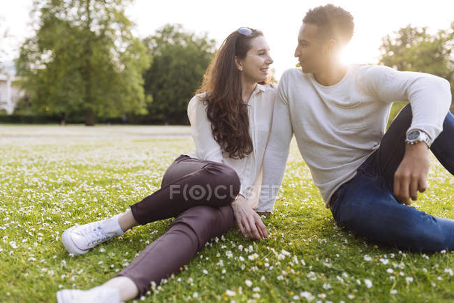 Jovem casal sentado na grama cara a cara sorrindo — Fotografia de Stock