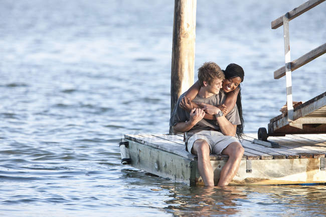 Jeune couple assis sur une jetée avec des pieds dans l'eau — Photo de stock