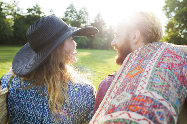 Vista posteriore di romantica giovane coppia che trasporta tappeto per pic-nic nel parco — Foto stock