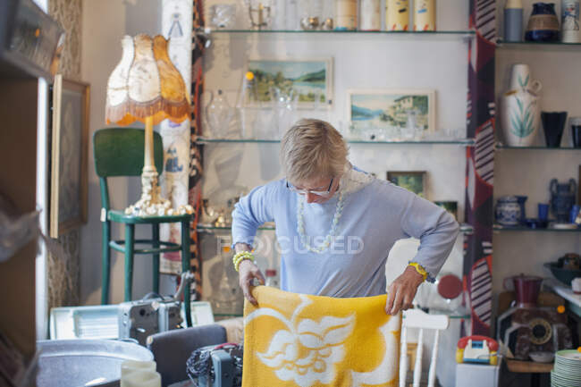Mulher madura dobrando cobertor amarelo na loja vintage — Fotografia de Stock