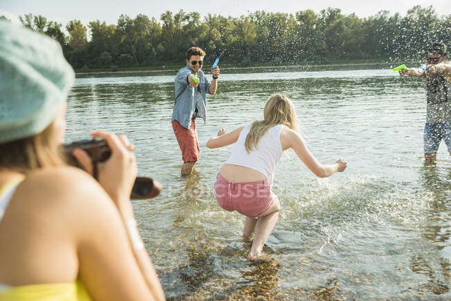 Amigos jugando con pistolas de agua en el lago - foto de stock