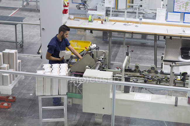 Trabajador masculino que utiliza la máquina en fábrica de embalaje de papel - foto de stock