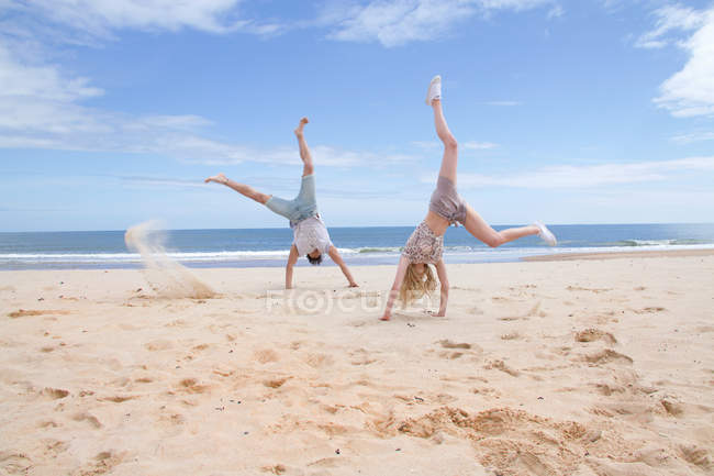 Pareja joven haciendo handstands en la playa - foto de stock