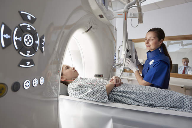 Mädchen im Grundschulalter geht in CT-Scanner mit Röntgenbildnerin und Mann im Hintergrund — Stockfoto