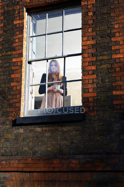Femme debout près de la fenêtre avec tasse — Photo de stock