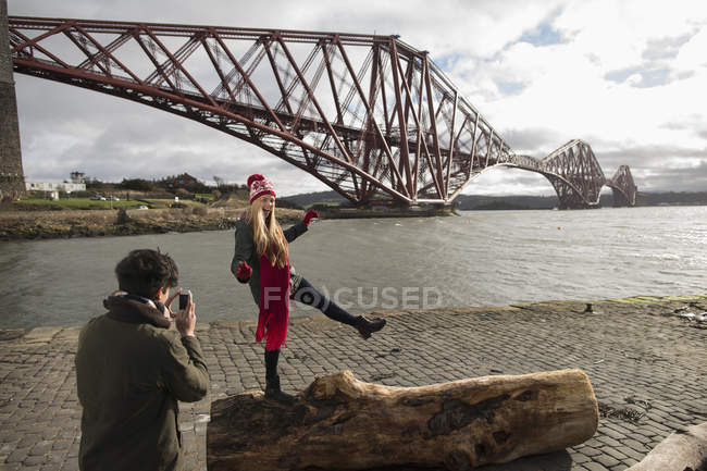 Una joven pareja posa frente al Forth Rail Bridge en Queensferry, cerca de Edimburgo, Escocia - foto de stock